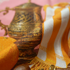 Mlle Ceinté Paris silk scarf, antique gold tankard, fresh orange, yellow striped fabric drape, wooden scrolls, salmon pink background still life.