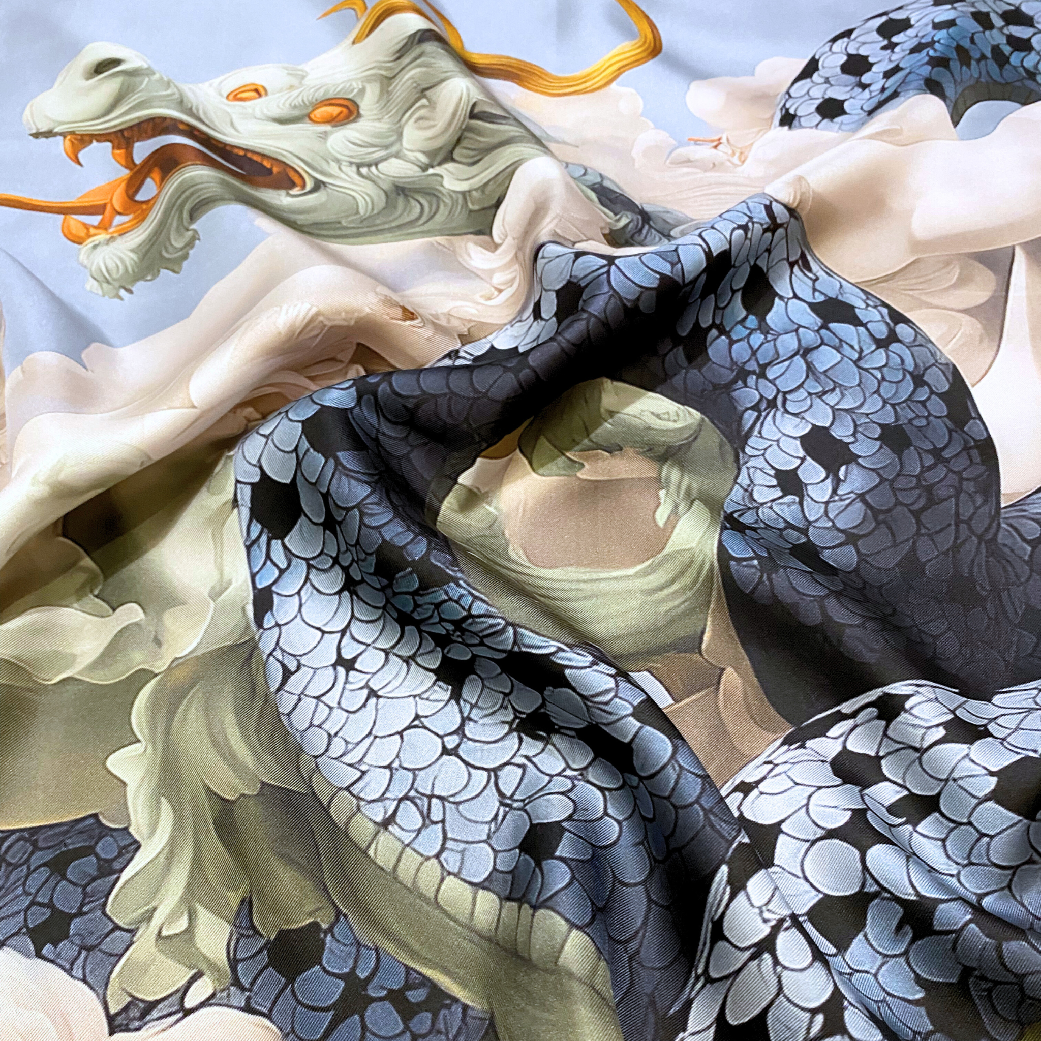 Mlle Ceinté Paris silk scarf, blue scaled dragon intertwining with classical marble statues, sky blue background with orange accents, hand-rolled hem.
