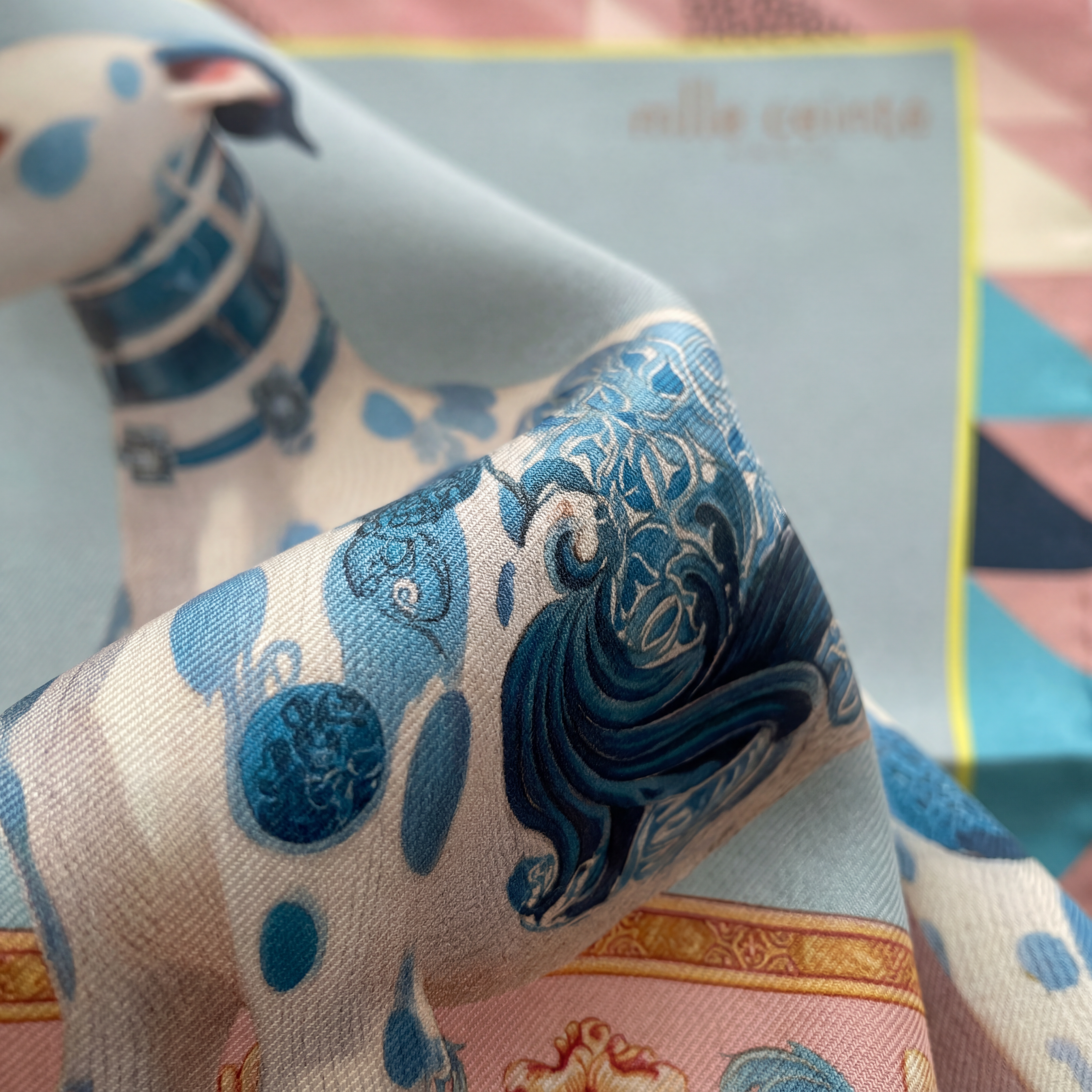 Mlle Ceinté Paris ipek eşarp, merkezde mavi beyaz porselen desenli aristokrat tazı figürü, pastel pembe zemin üzerinde romantik çiçekler ve neon yeşil şeritli lüks şal.
Mlle Ceinté Paris silk scarf, central aristocratic hound figure with blue and white porcelain pattern, surrounded by romantic flowers on a powder pink background with neon green border.